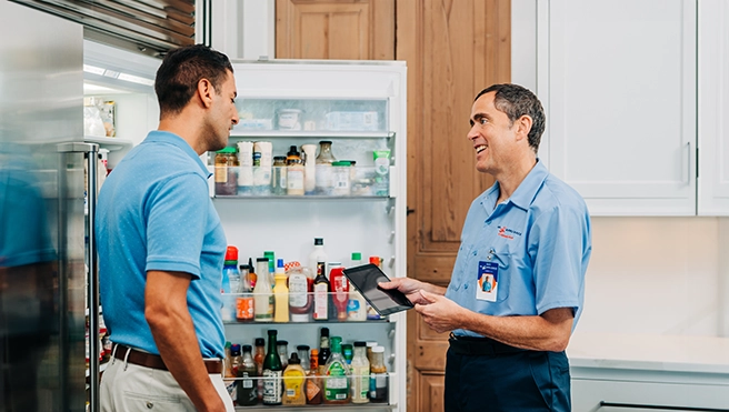 A Mr. Appliance technician talks to a customer in front on an open refrigerator.