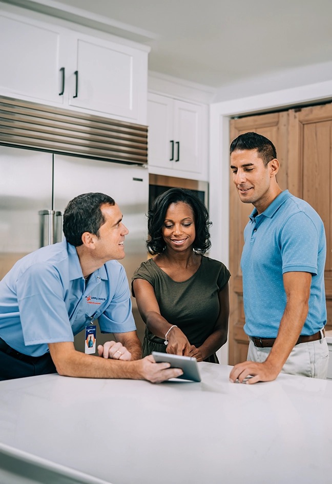 A Mr. Appliance technician talking with customers at a kitchen island.