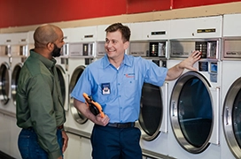 Mr. Appliance service professional discussing with customer in front of rows of commercial dryers.