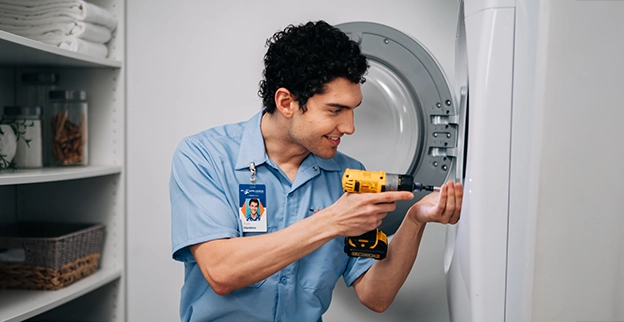 Mr. Appliance service professional smiling as using drill on dryer door.