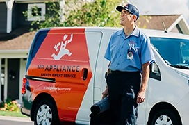 Male Mr. Appliance service technician with tool bag standing in front of branded van.