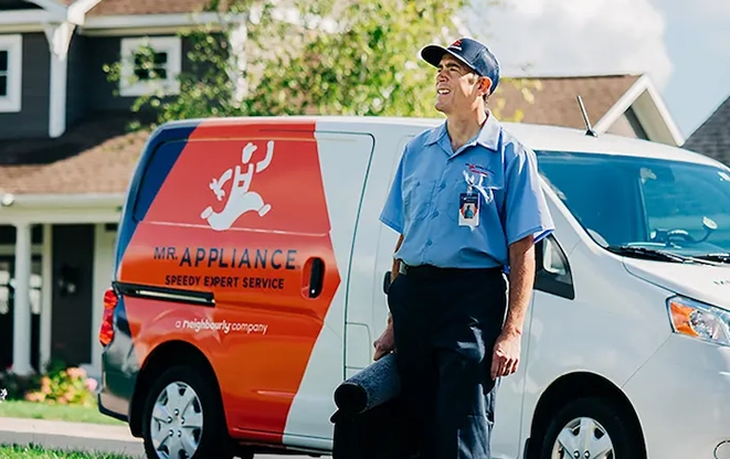 Male Mr. Appliance service technician with tool bag standing in front of branded van.