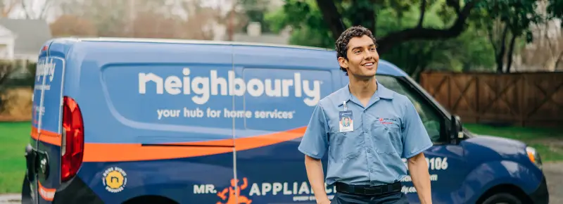 Smiling male Mr. Appliance service technician with tool bag walking away from landscaped residential home.