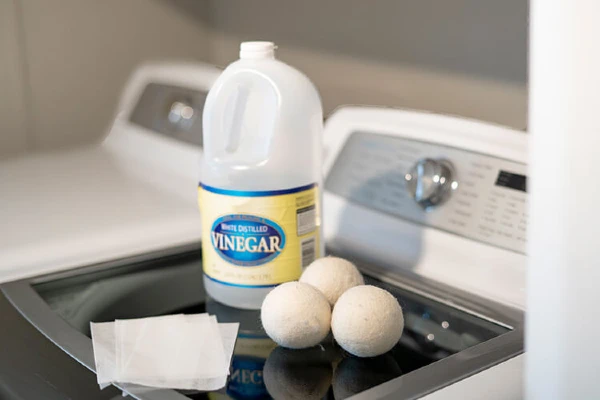 Dryer sheets, dryer balls, and a bottle of vinegar on top of a dryer
