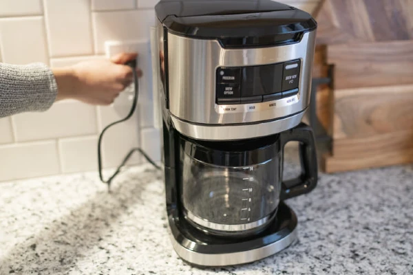 A person pulling the cord of a coffee maker out of an electrical outlet