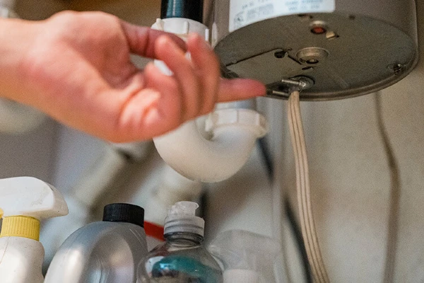 A person reaching for the garburator reset button at the bottom of the device