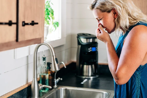 A woman standing over the sink holding her nose