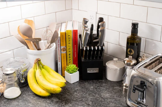 Bananas, utensils, cookbooks, a knife set, a toaster, and other items in the corner of a kitchen countertop