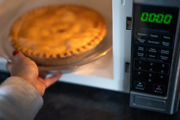 A person taking a pie out of a convection microwave