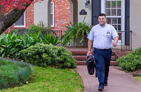 Male Mr. Appliance service technician with tool bag walking away from landscaped residential home.