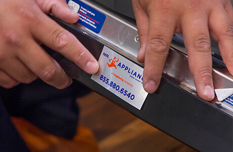 Technician placing Mr. Appliance service reminder sticker on appliance.