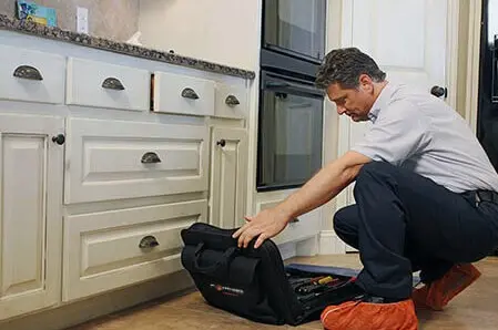 Male Mr. Appliance technician in residential kitchen unpacking toolkit.